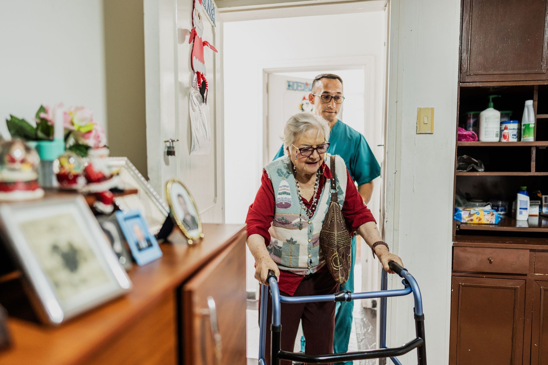 Caregiver helping senior woman walk with walker at home.