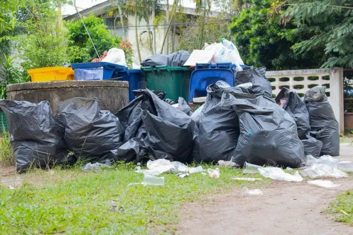 Large black garbage bags and bins piled for residential waste pickup.
