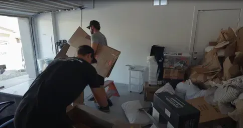 Workers clearing cardboard boxes and clutter from a residential garage.