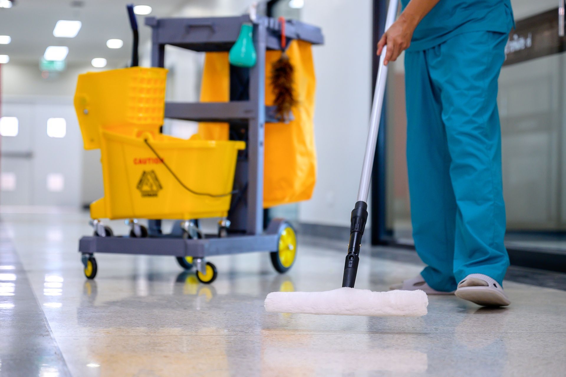 Custodian mopping a shiny hallway floor with a yellow bucket and cleaning cart.
