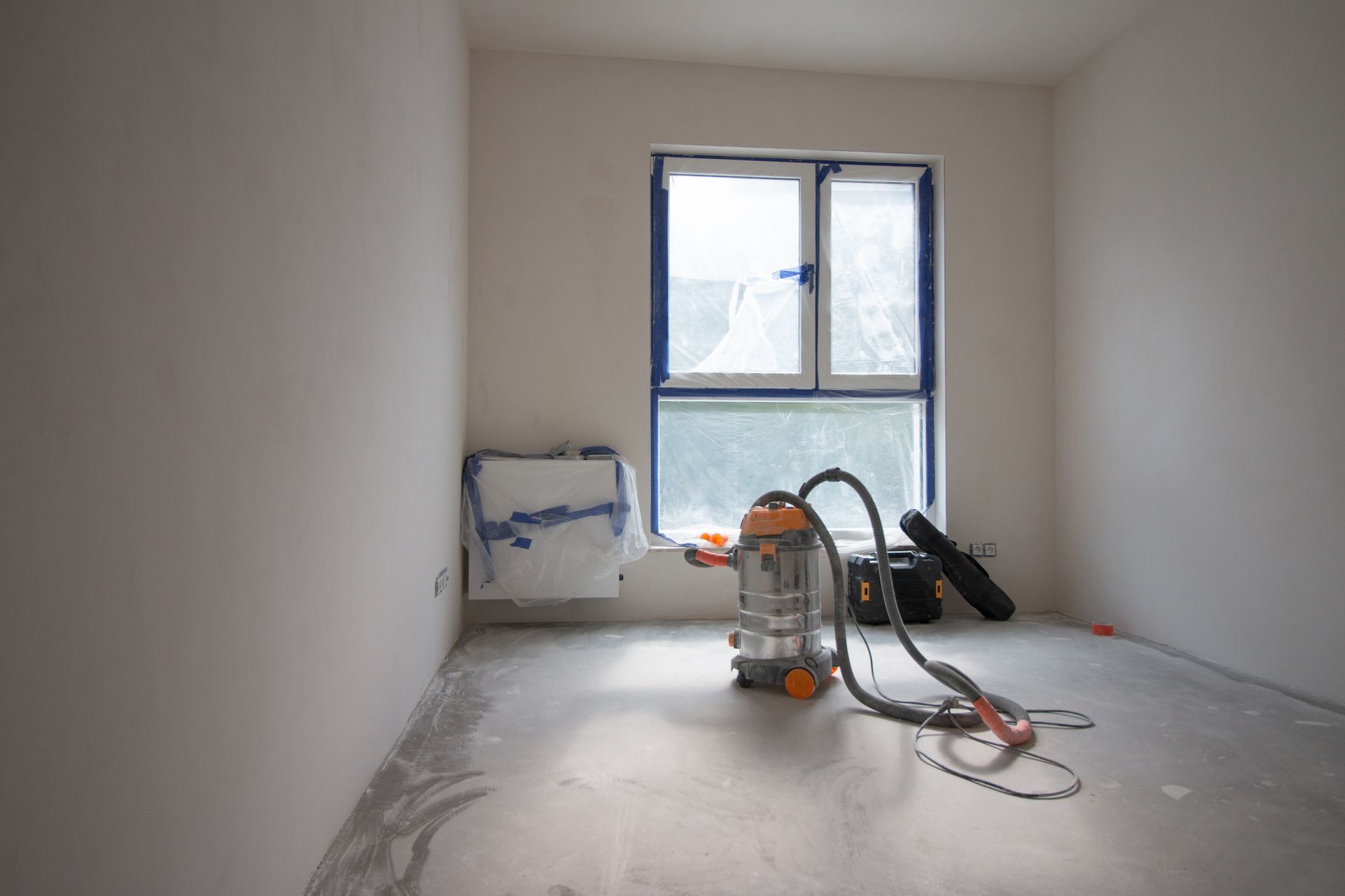 Empty room with a window, construction debris, and a vacuum cleaner.