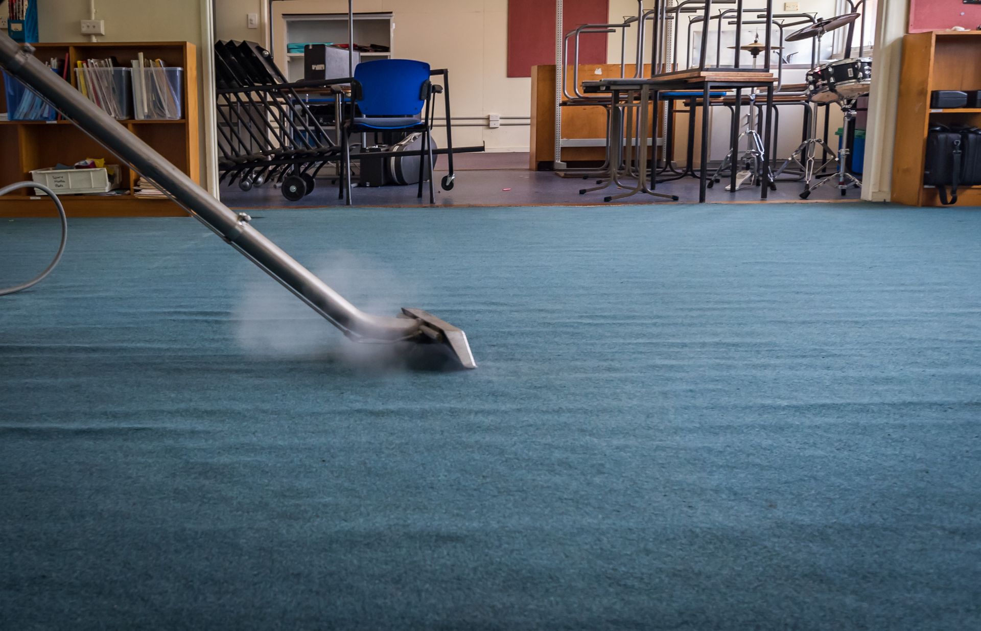 Steam cleaner cleaning blue carpet in a room with chairs and bookshelves.