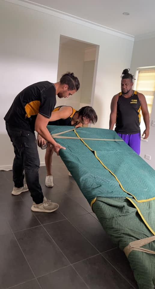 A Group of Men Are Moving a Large Piece of Furniture in a Living Room — GNQ Removals–Transport–Storage In Portsmith, QLD