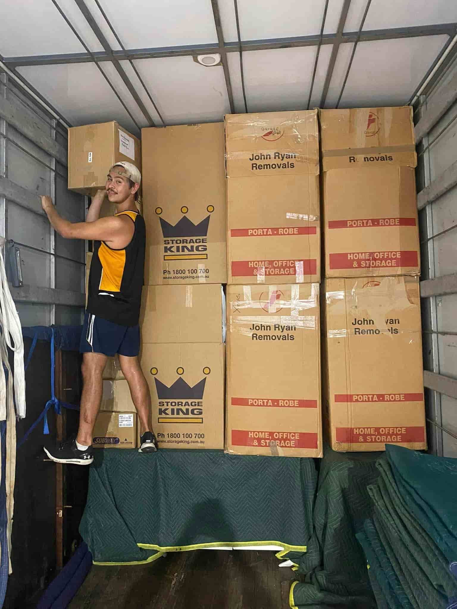 A Man is Standing in the Back of a Moving Truck Holding a Box — GNQ Removals–Transport–Storage In Portsmith, QLD
