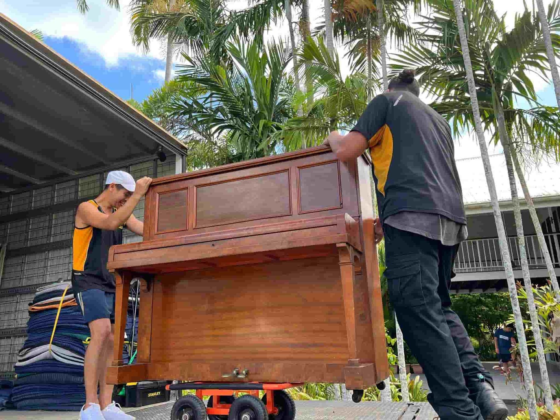 Two Men Are Carrying a Piano on a Dolly — GNQ Removals–Transport–Storage In Portsmith, QLD