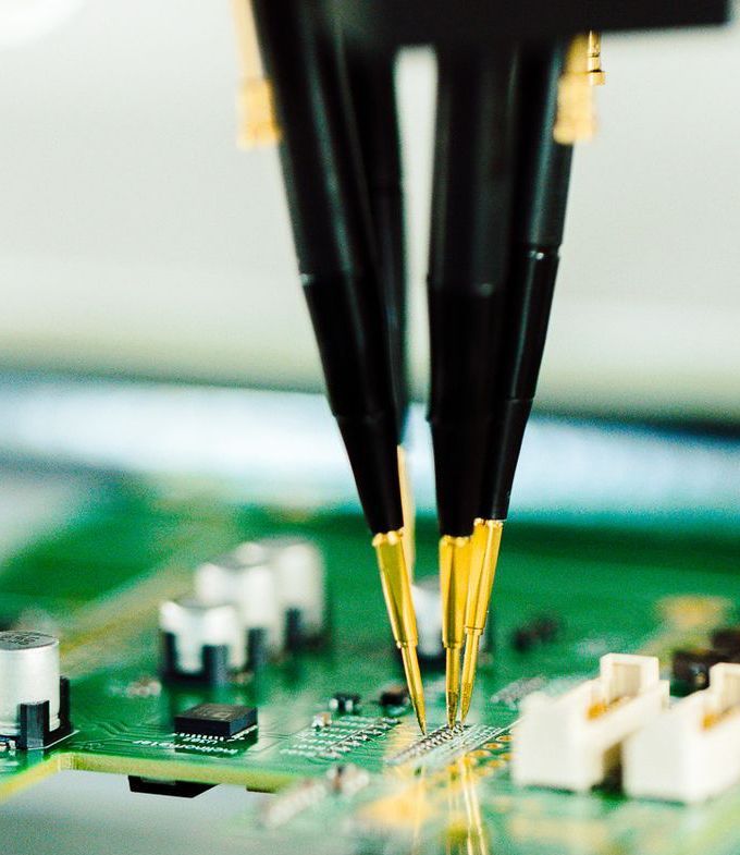 Testing probes touching a green circuit board, conducting electronic measurements.