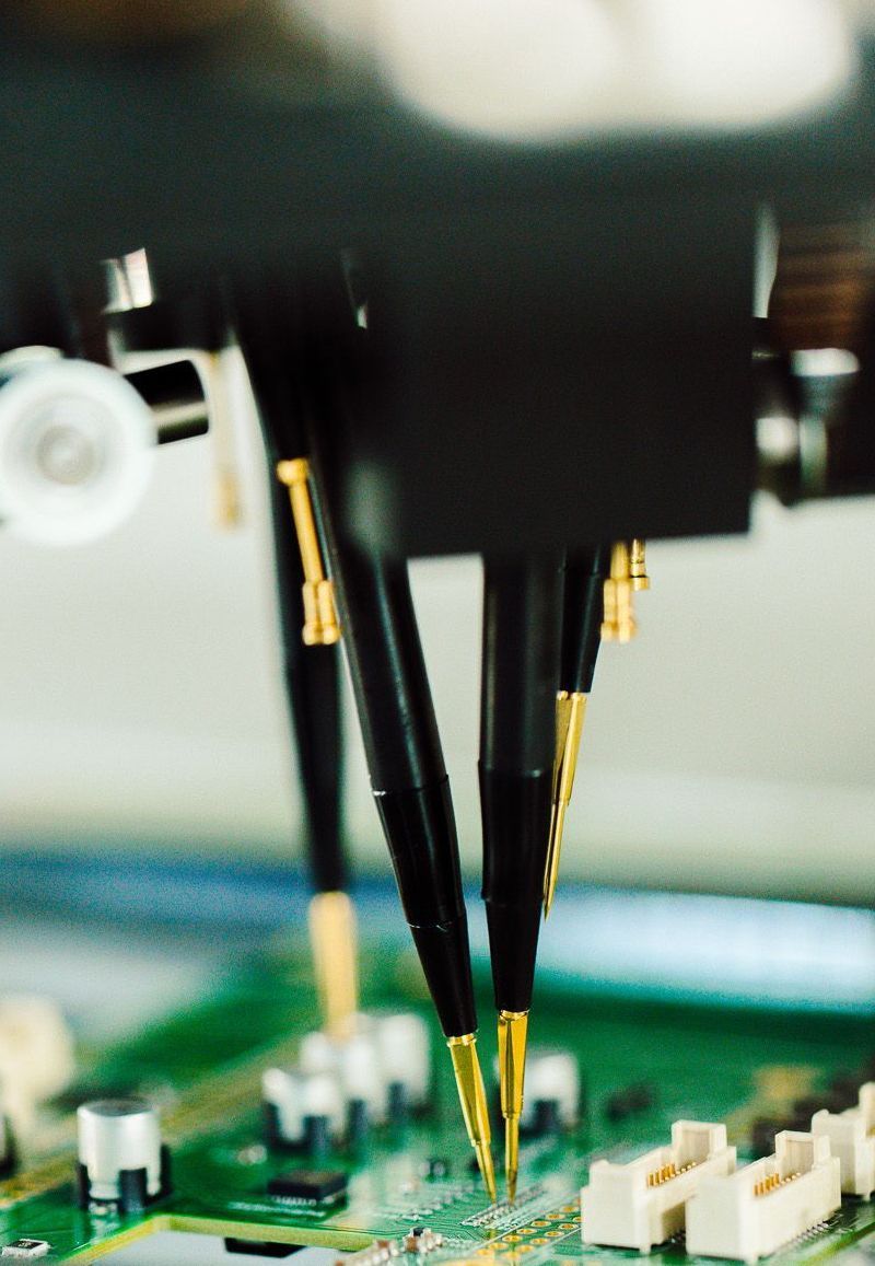 Probes testing a circuit board; black and gold tools touching green surface.