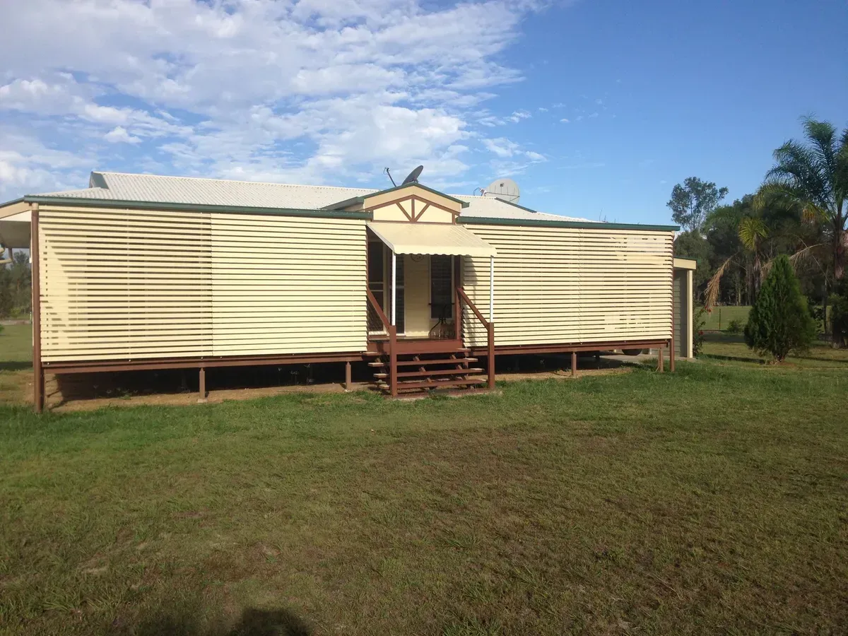 A Weathered, Beige Corrugated Iron House on Stilts in A Grassy Field, with A Blue Sky — Wares Blinds, Screens & Awnings In Gladstone Central, QLD