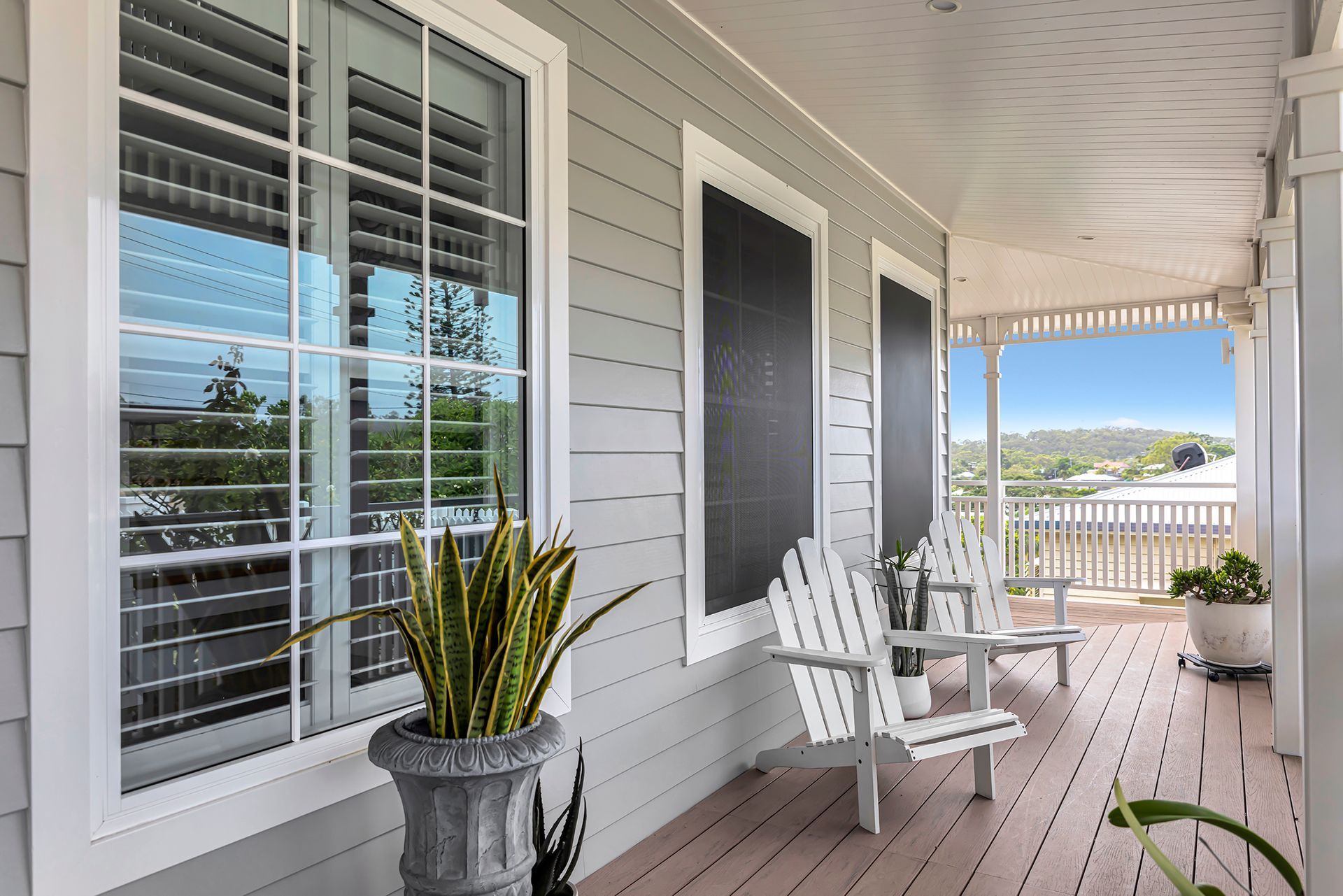 Porch with white chairs, shutters, grey siding, and potted plants.