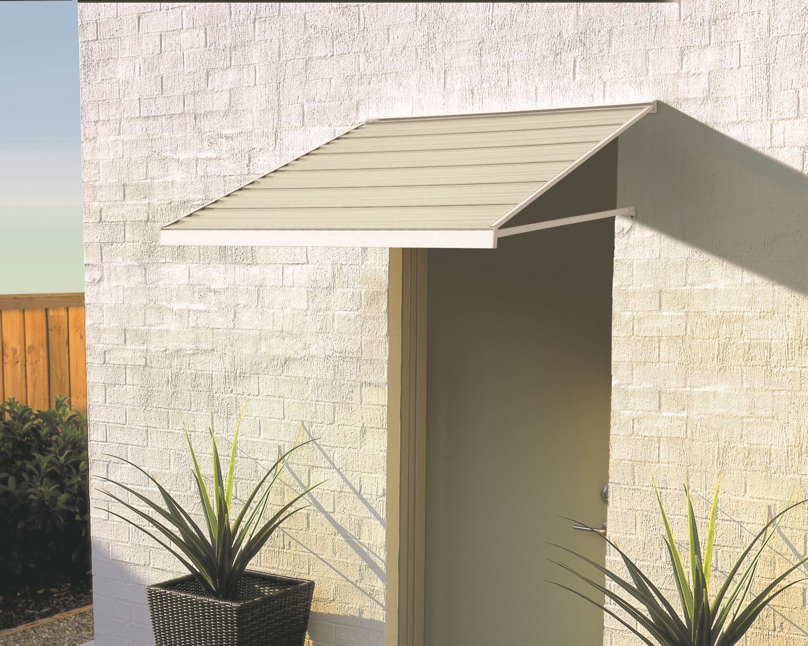 Beige awning over a white door on a textured wall; plants are in front.
