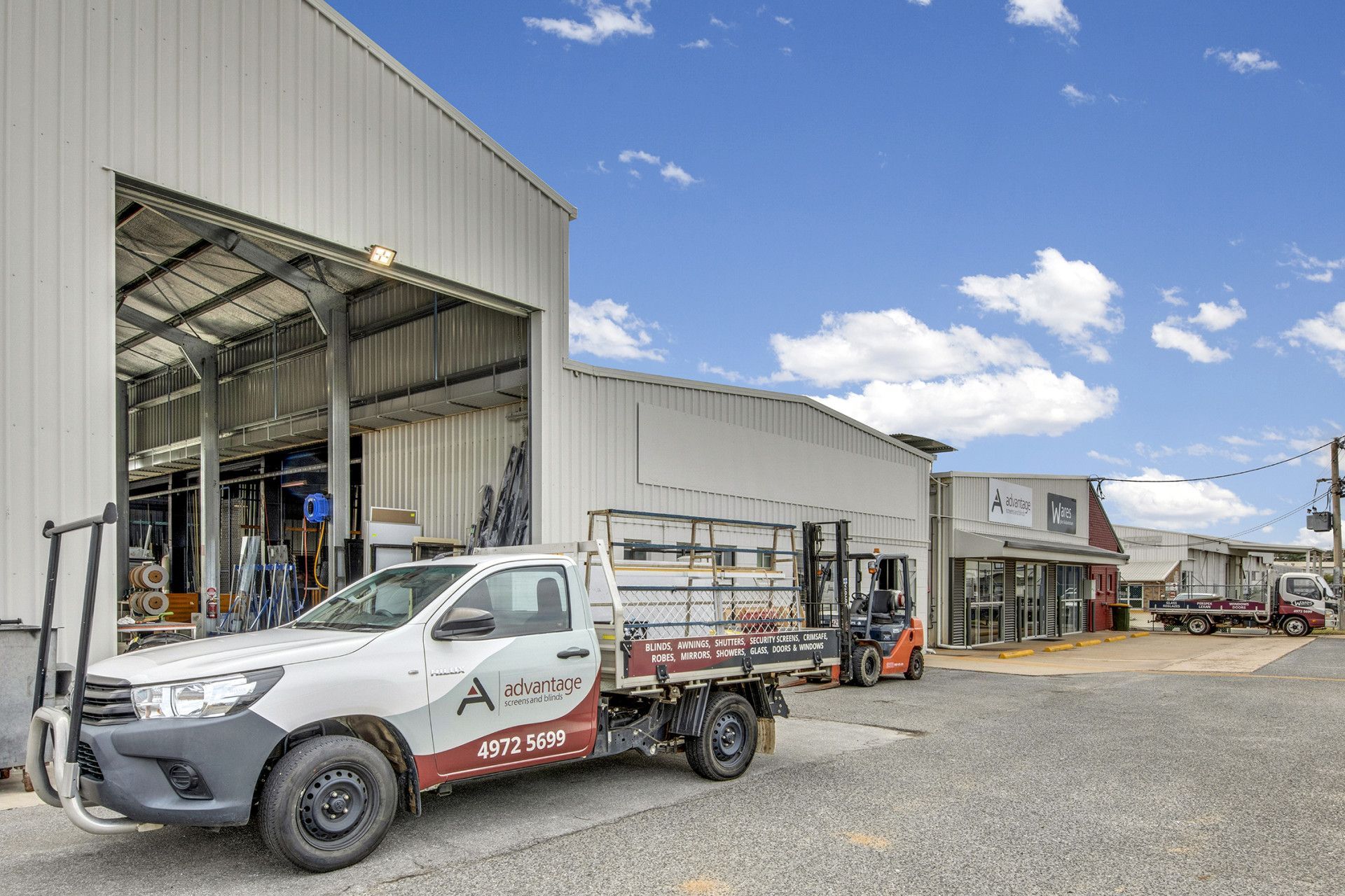 Truck parked in front of warehouse with open bay, other businesses in background.