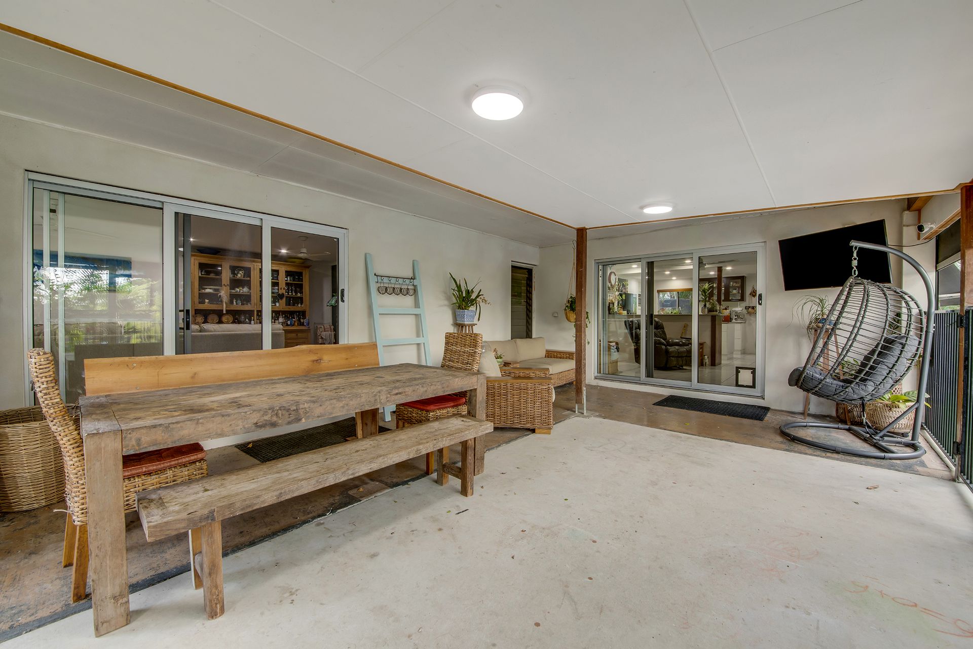 Covered patio with a wooden table and bench, plus seating, and sliding glass doors.