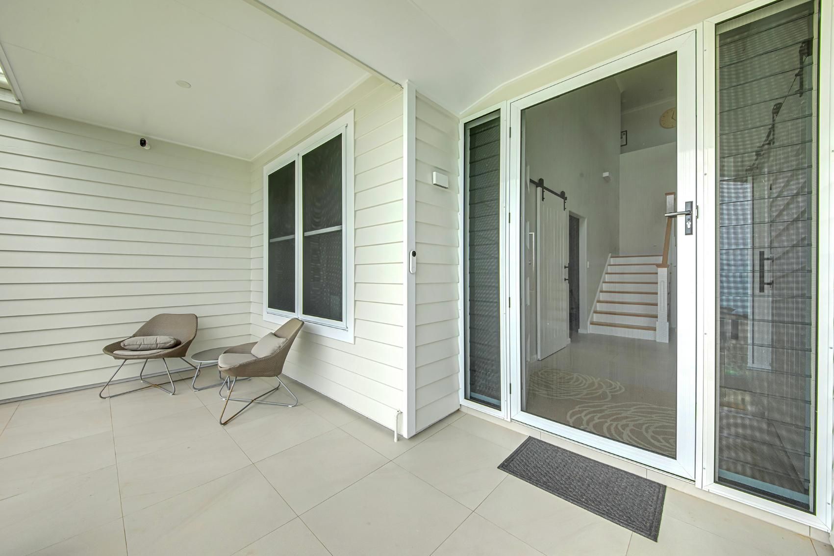 A Covered Patio with Two Chairs, a Window, and Glass Doors Leads to Stairs Inside a Building — Wares Blinds, Screens & Awnings In Yeppoon, QLD