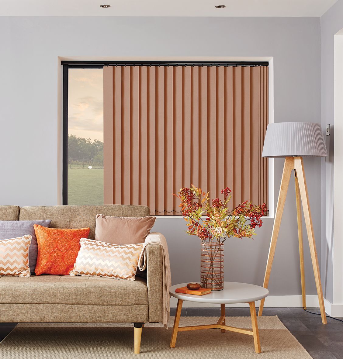 Living room with beige sofa, patterned pillows, round table, floor lamp, and vertical blinds.