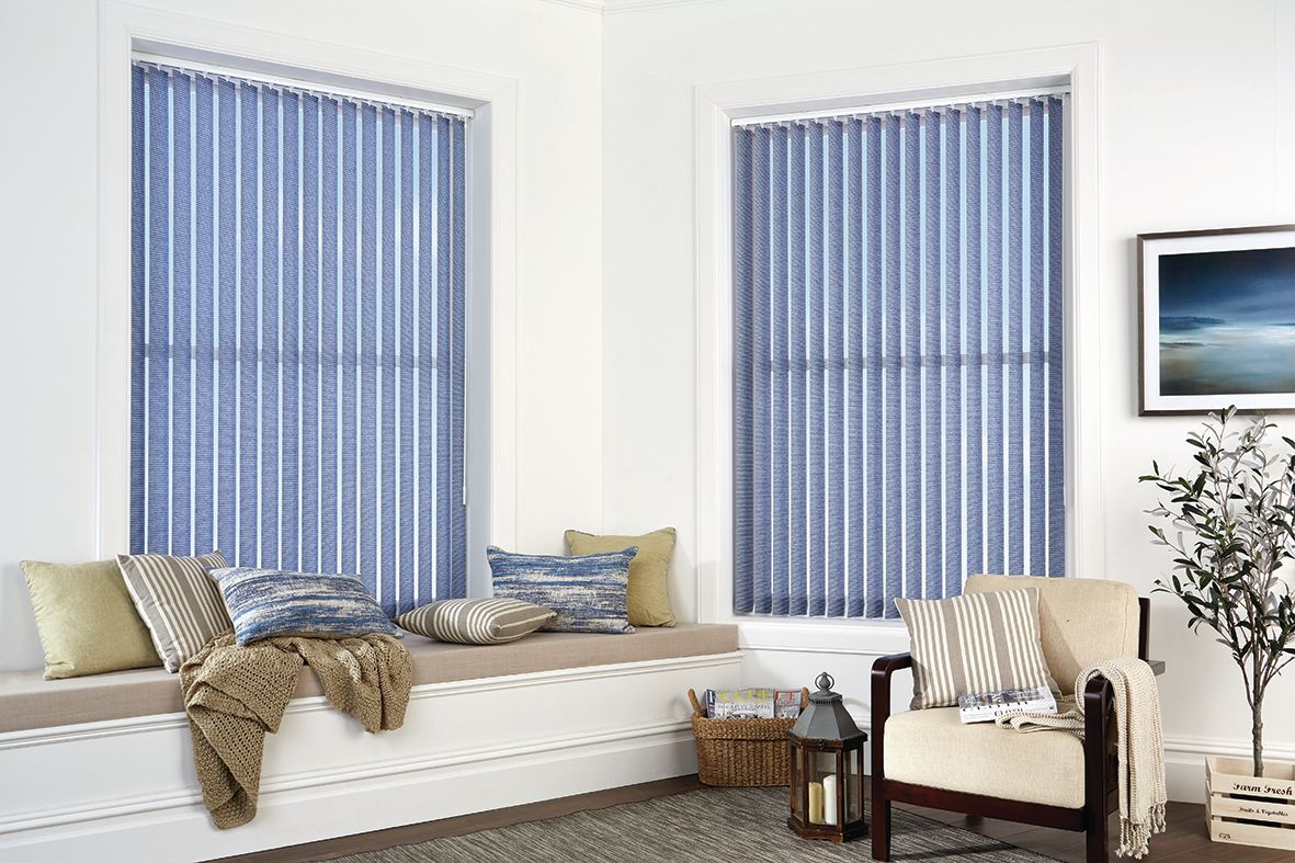 Living room corner with blue vertical blinds, window seat with pillows, chair, and a framed seascape.
