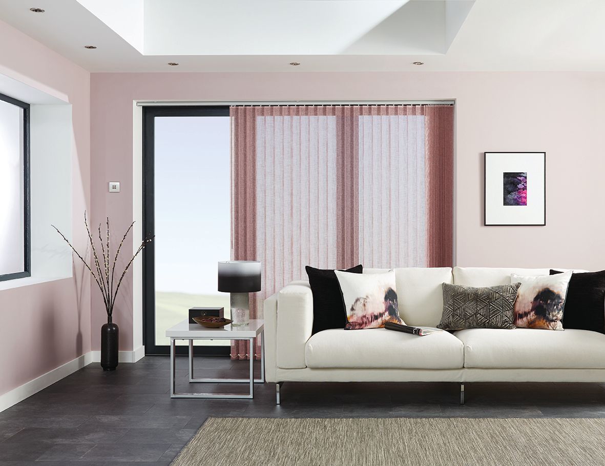 Living room with white sofa, pink walls, large window with sheer blinds, and dark rug.
