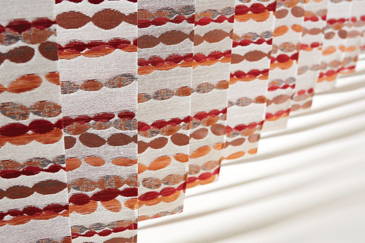 Close-up of patterned vertical blinds in shades of brown and orange, casting shadows.
