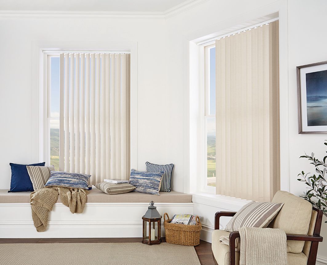 Interior of a room with vertical blinds. Window seat with pillows, chair, basket, and picture frame.