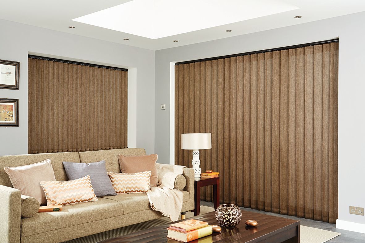 Living room with brown vertical blinds covering windows, sofa with pillows, and side table with lamp.