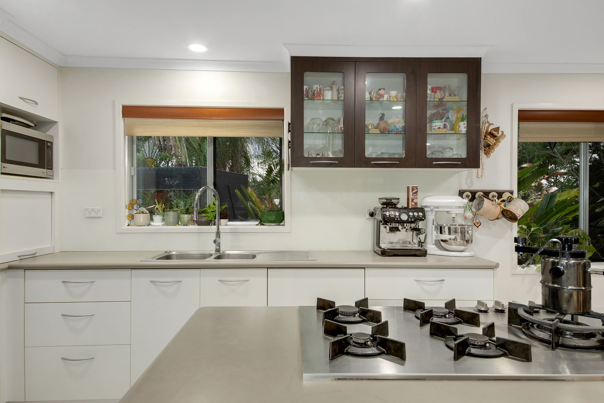 Modern kitchen with white cabinets, stainless steel stovetop, and dark upper cabinets with glass doors.