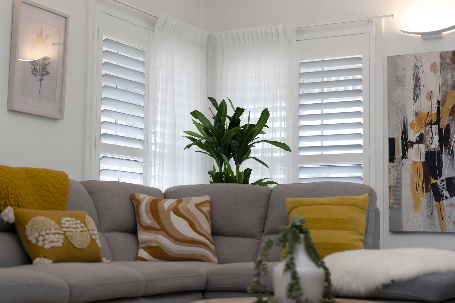 Cozy living room with gray sectional sofa, white shutters, and decorative pillows in shades of yellow and brown.