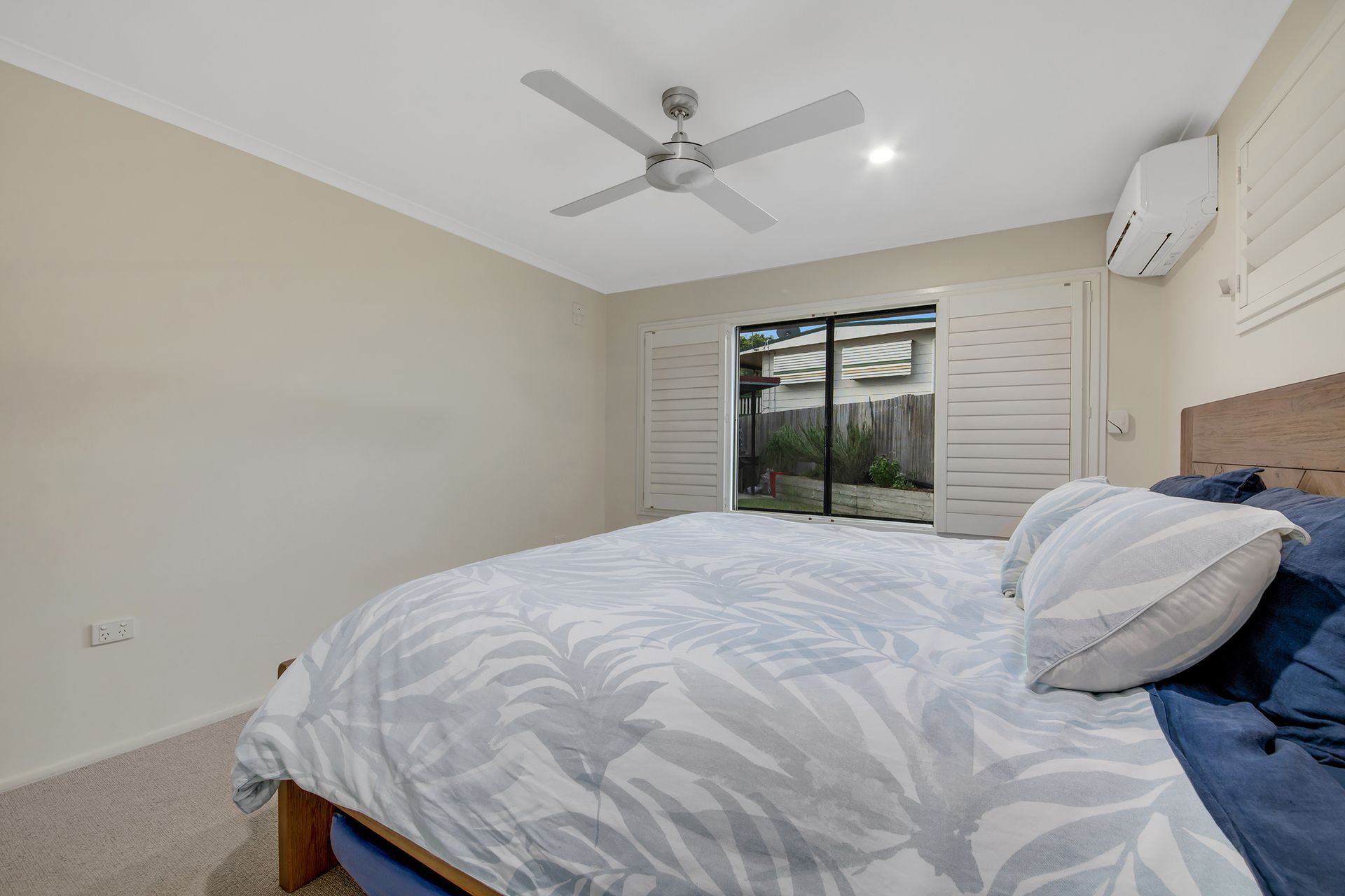 Bedroom With a Bed, Open Window With Shutters, Ceiling Fan, and Air Conditioner — Wares Blinds, Screens & Awnings In Gladstone Central, QLD