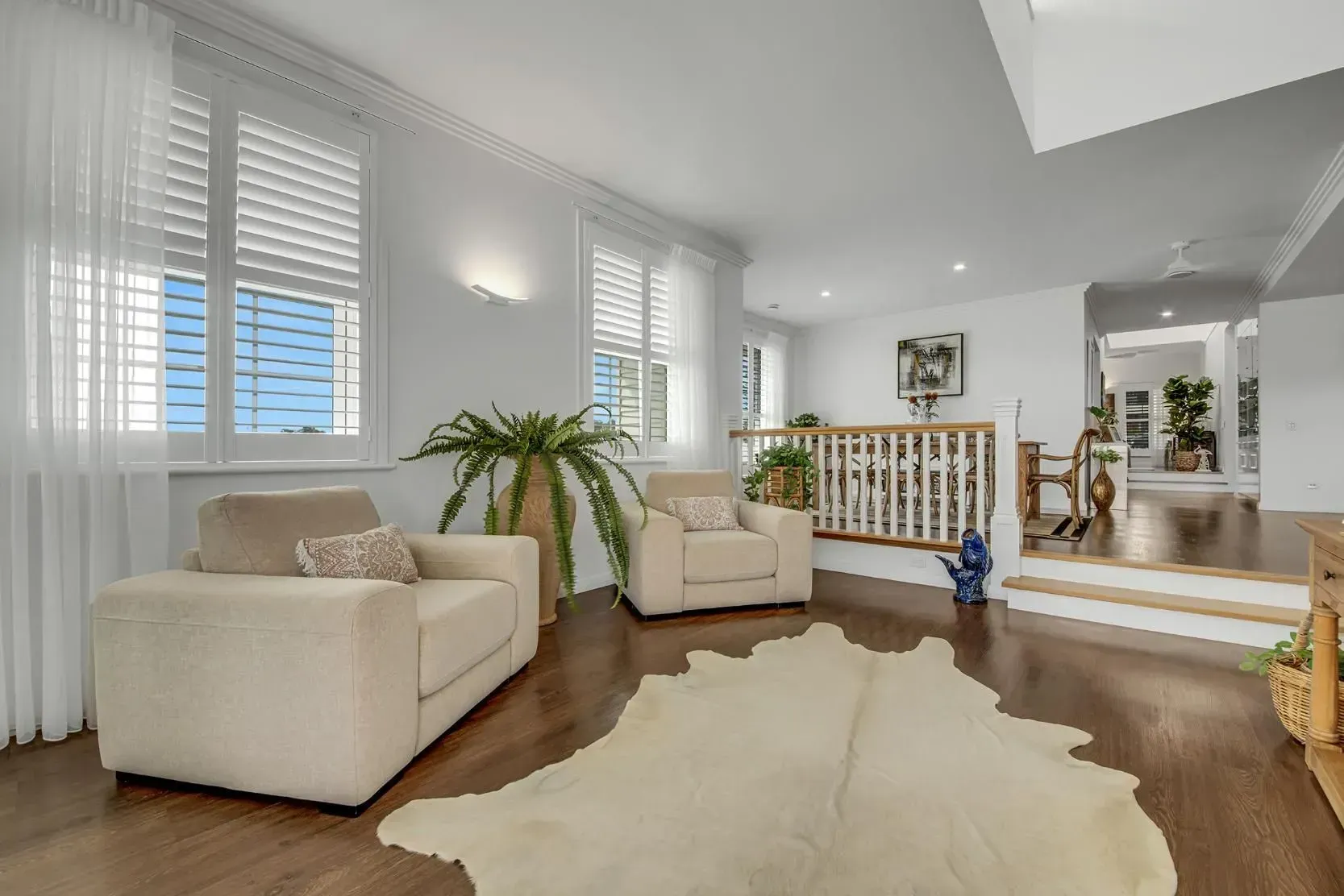 Living Room with Two Beige Armchairs, Cowhide Rug, and Wooden Floors. Bright Windows and Stairwell — Wares Blinds, Screens & Awnings In Gladstone Central, QLD