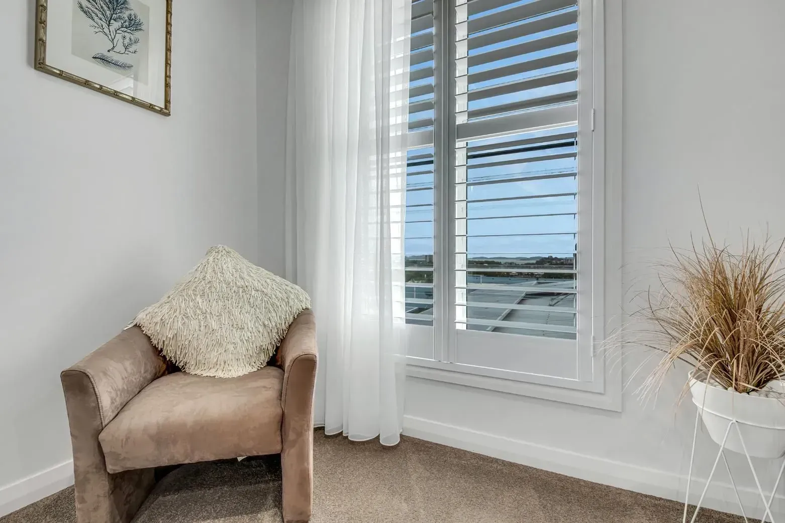 A Cozy Reading Nook with A Beige Armchair, White Curtains, and Window with Shutters — Wares Blinds, Screens & Awnings In Gladstone Central, QLD
