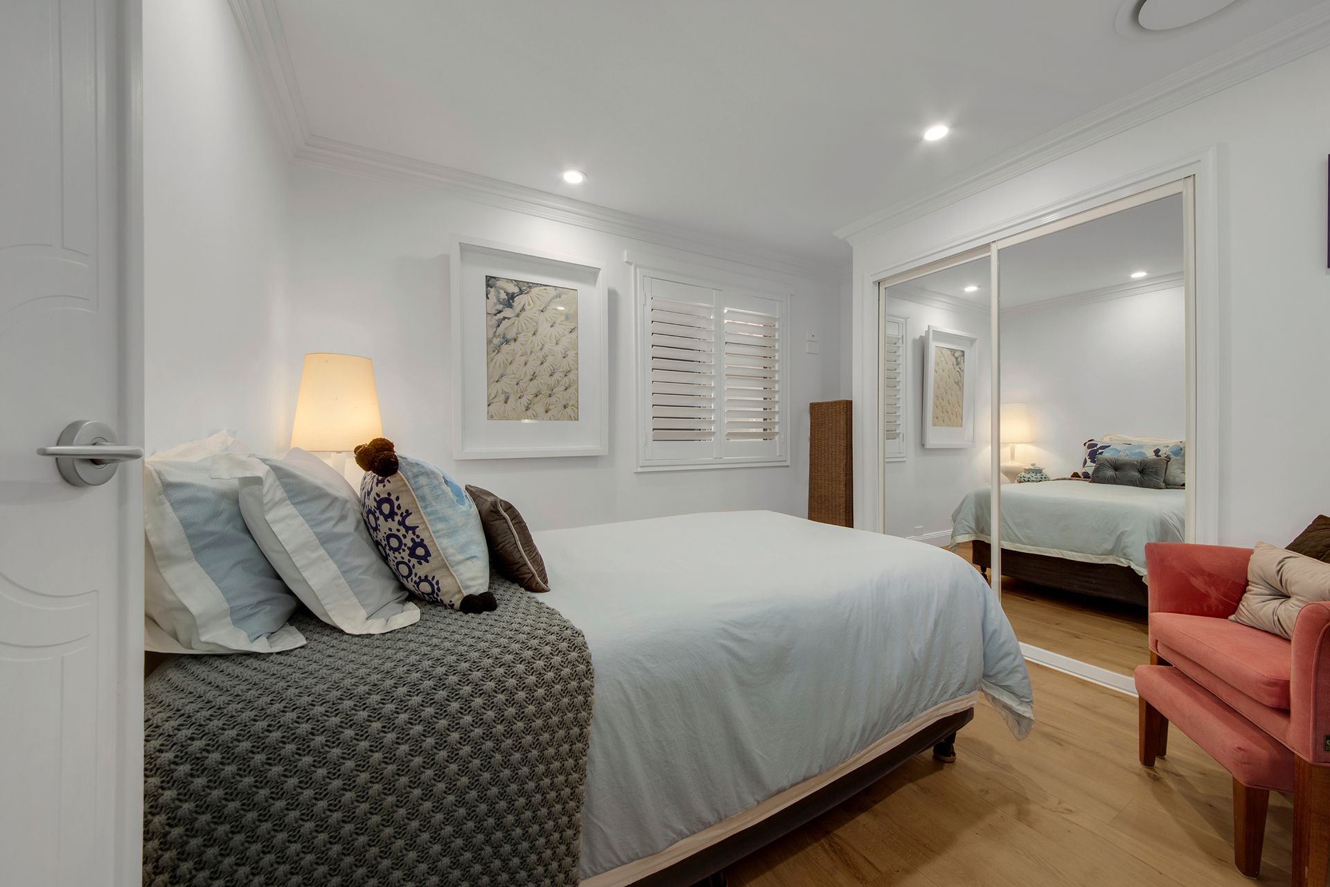 Bedroom with bed, pillows, and a mirrored closet; red armchair in the corner.