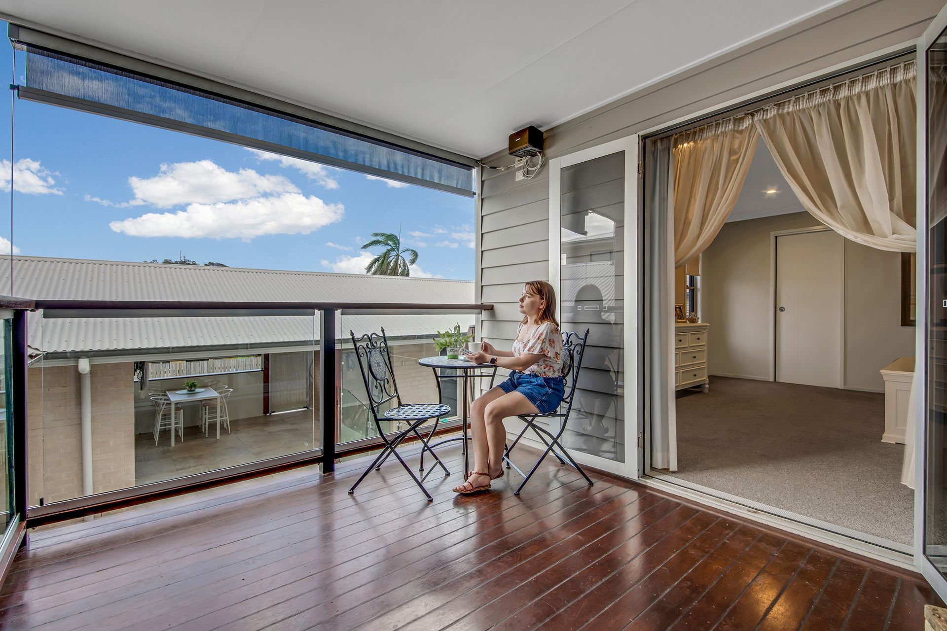 Woman Seated on Balcony with Table and View, Sliding Door to Room — Wares Blinds, Screens & Awnings In Gladstone Central, QLD