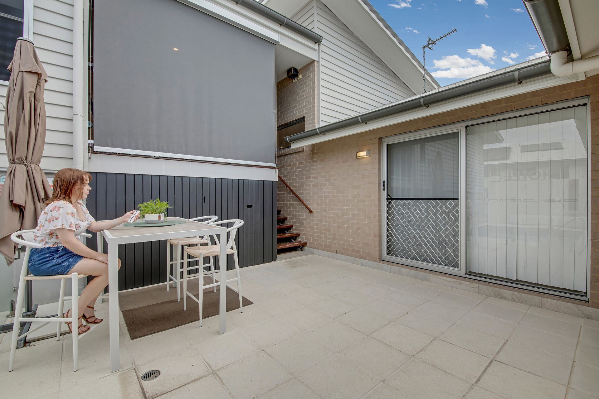 Woman sitting at table on patio under awning; sliding glass door visible.