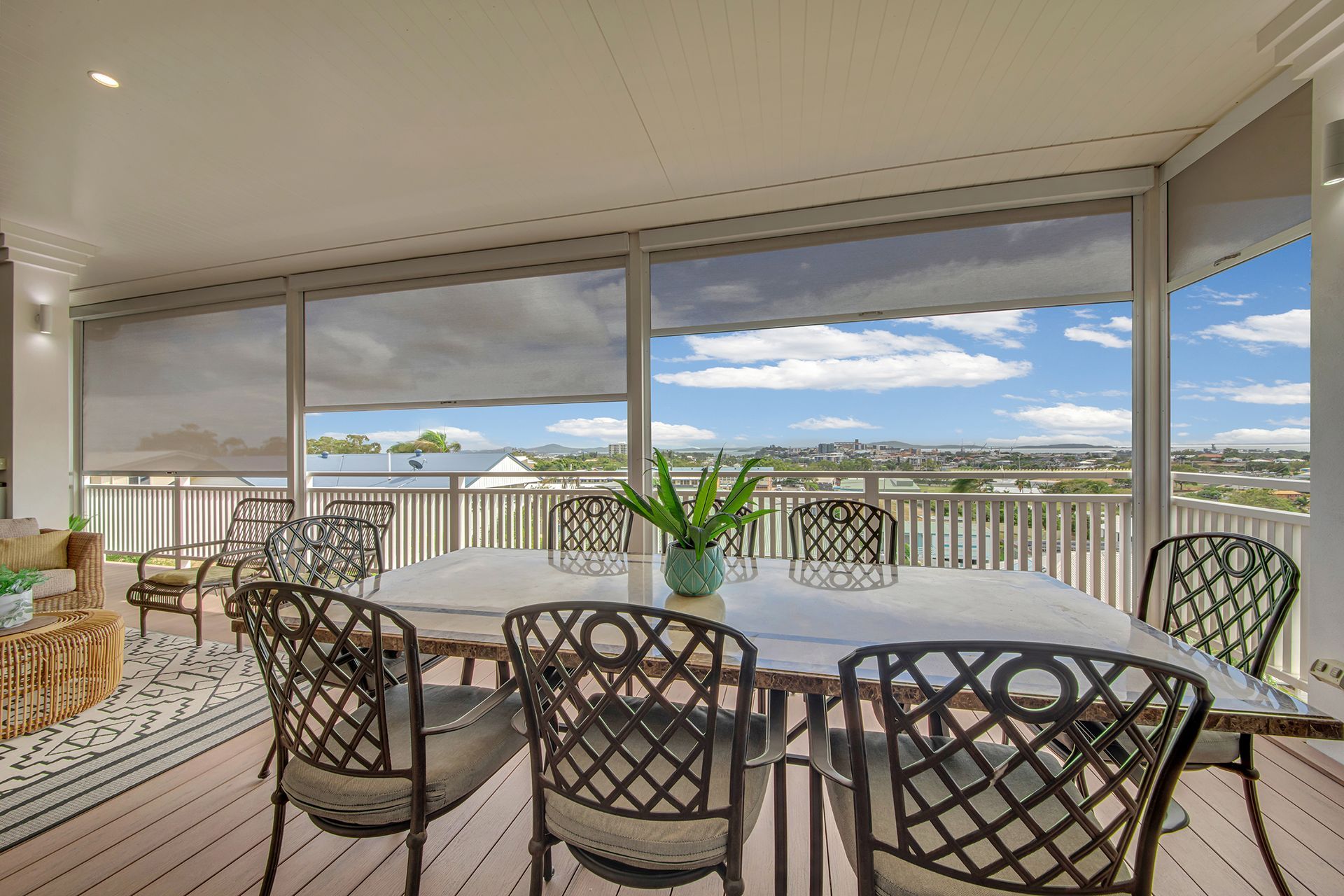 Outdoor dining area with table, chairs, and partial sun shades overlooking a city view.