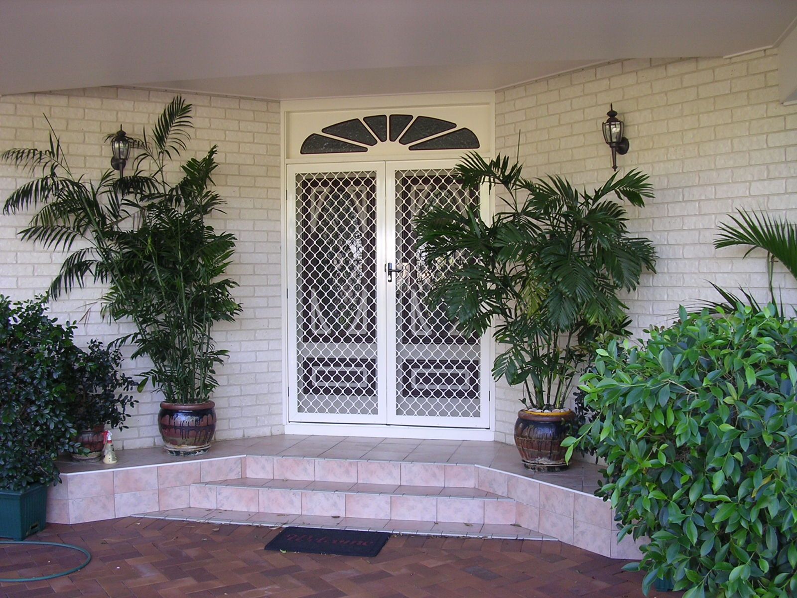 White double doors with screen, flanked by potted plants, on brick porch.