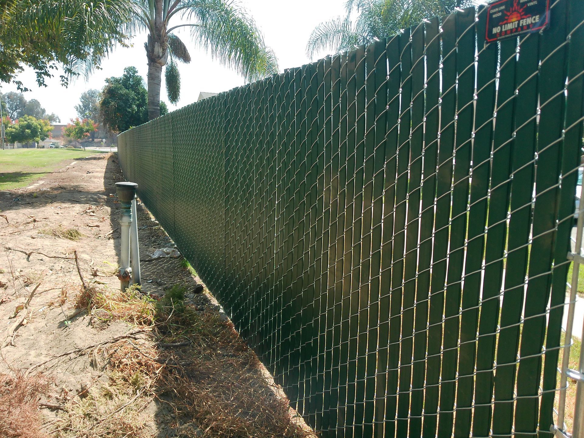 A chain link fence with a green slat covering it.