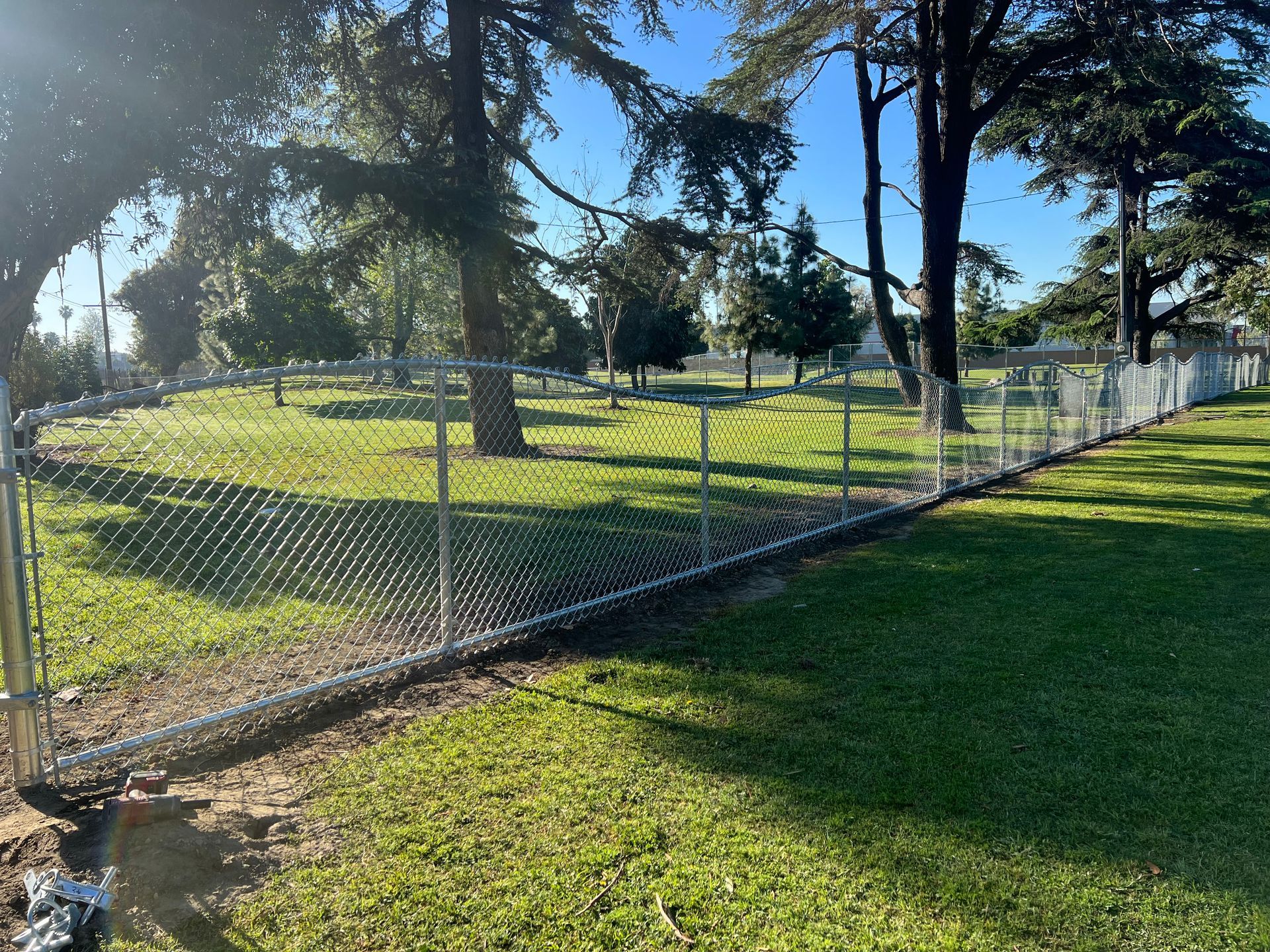 A chain link fence surrounds a grassy field with trees in the background.