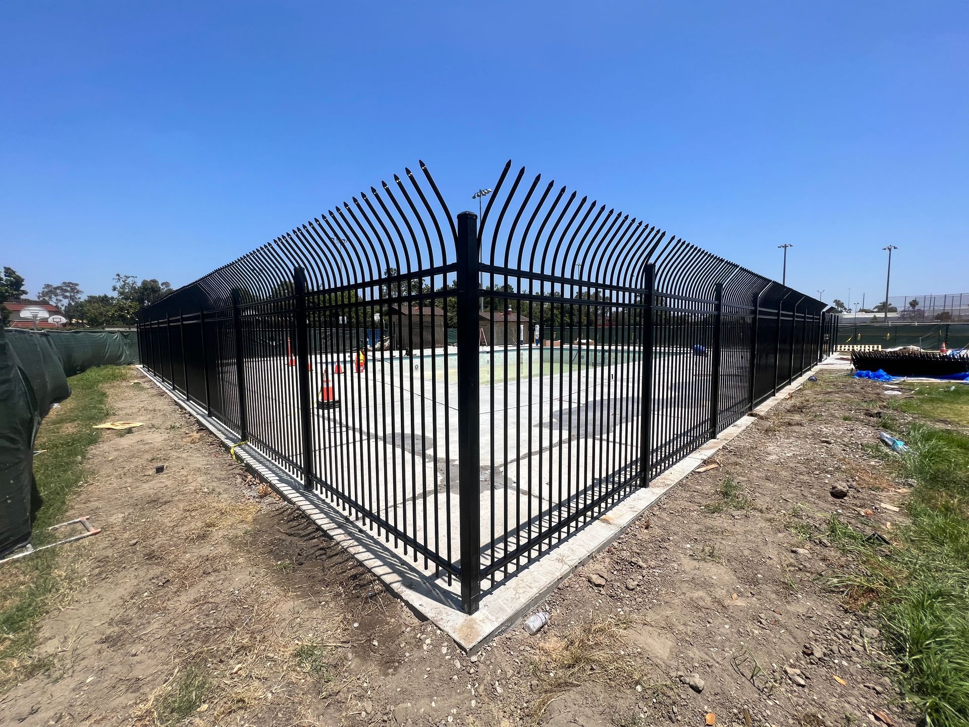 A black metal fence is surrounding a swimming pool.