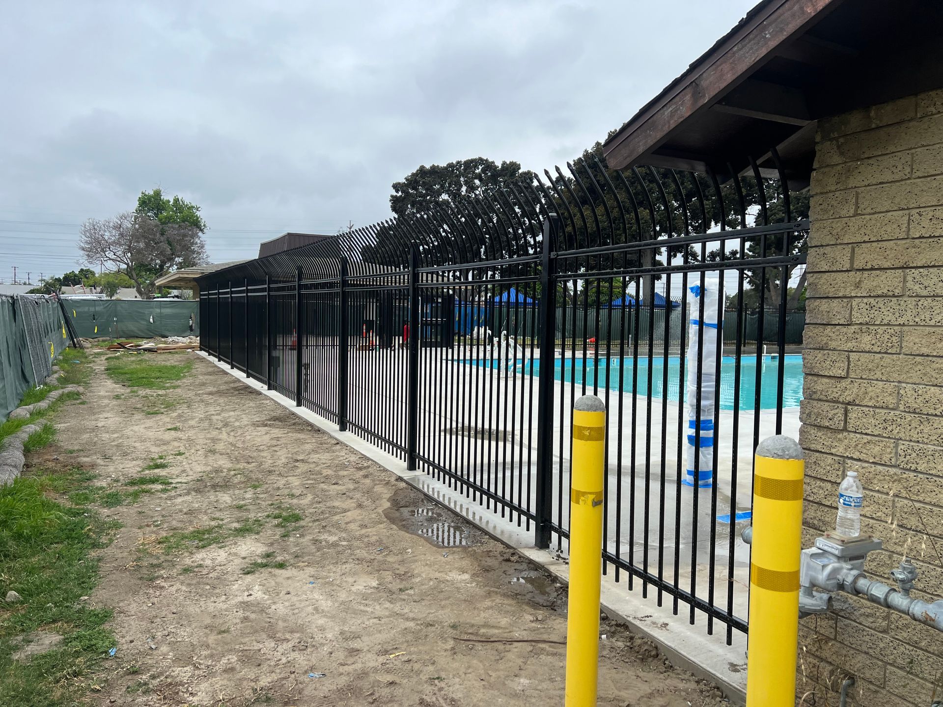 A metal fence surrounds a swimming pool next to a brick building.