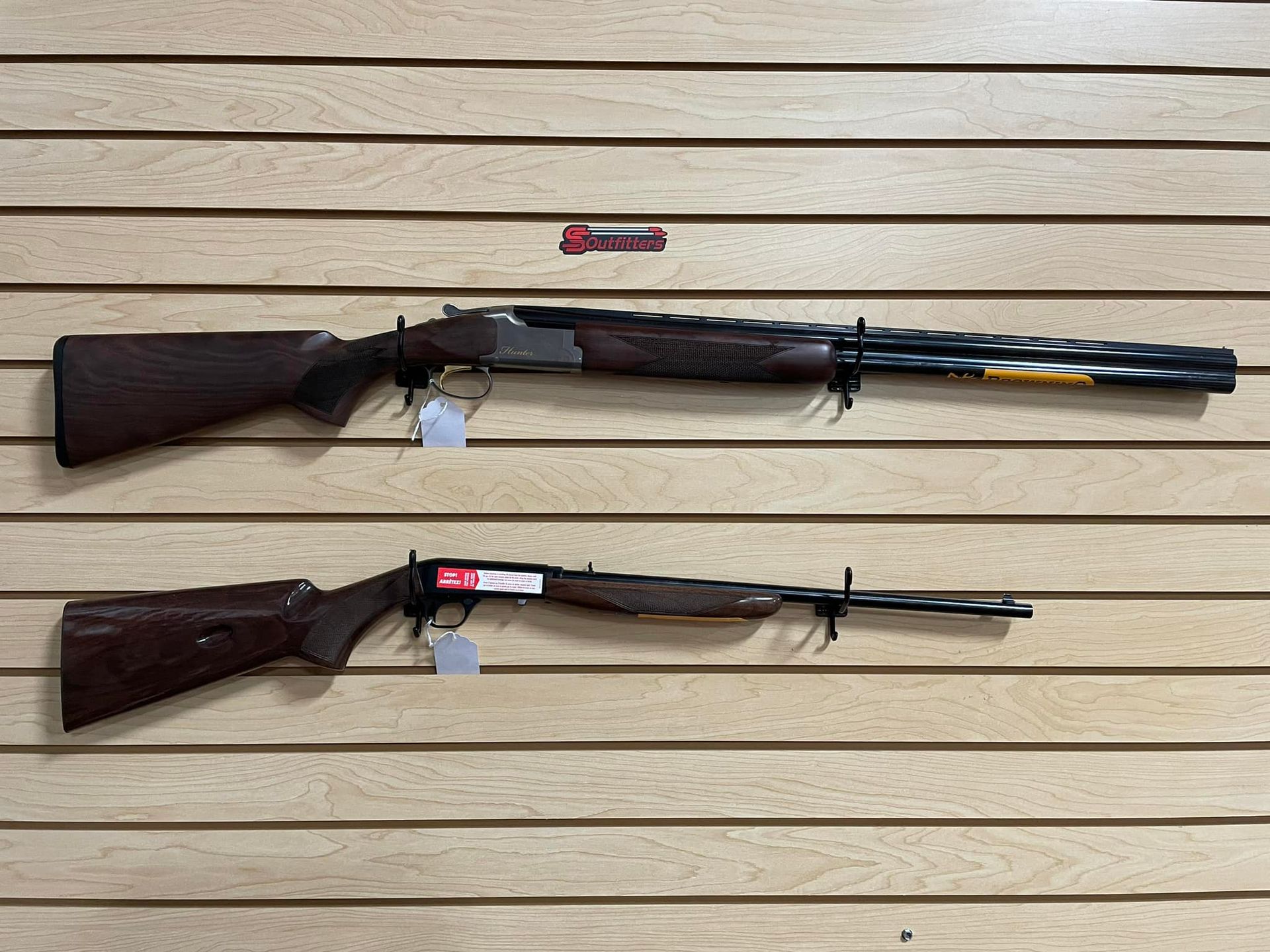 Two shotguns are hanging on a wooden wall.