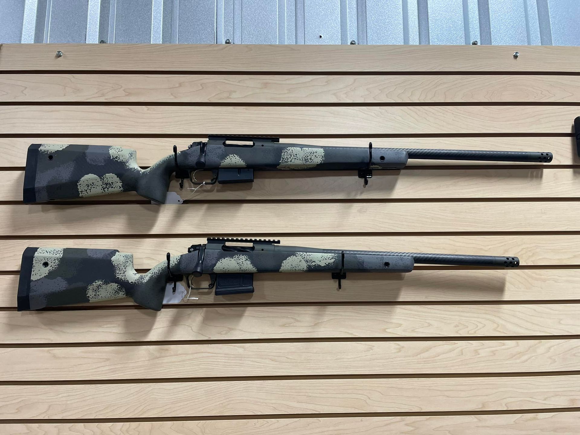Two sniper rifles are hanging on a wooden wall.