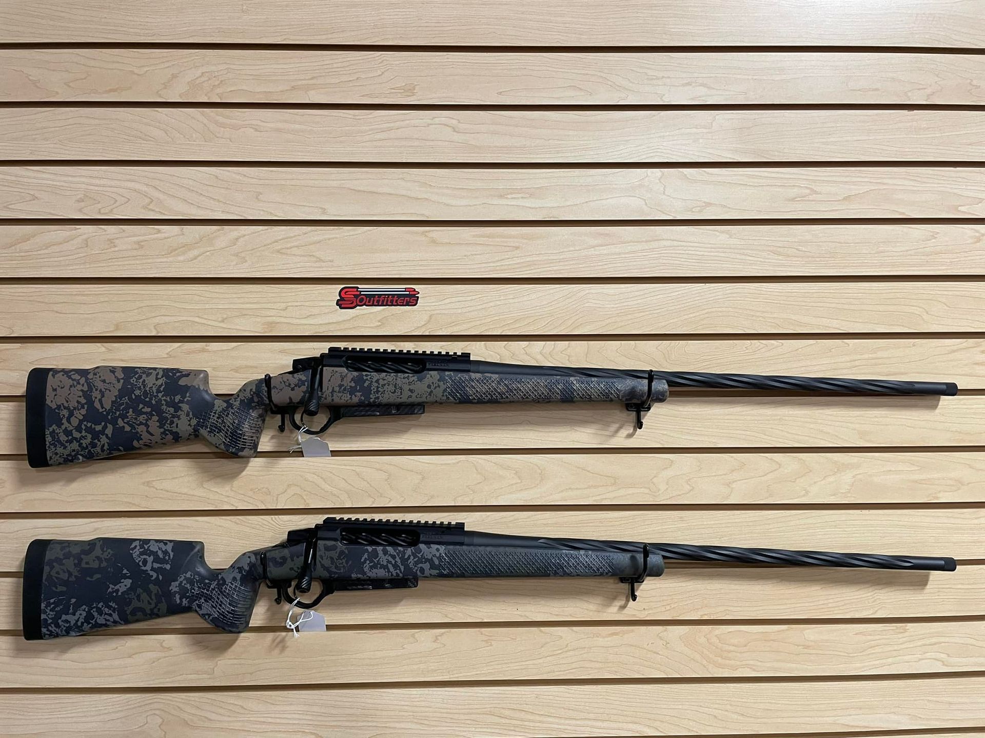 Two sniper rifles are hanging on a wooden wall.
