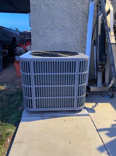 A large air conditioner is sitting on a sidewalk next to a building.