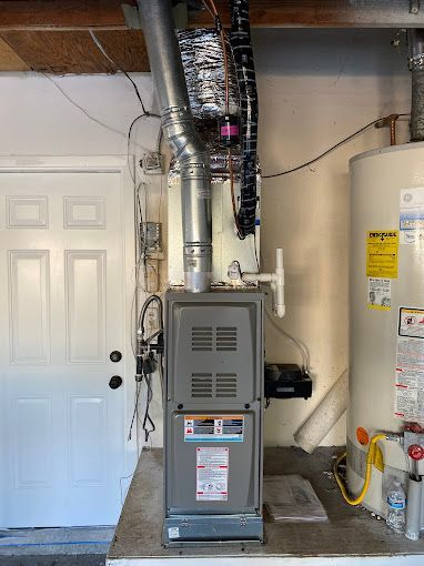 A gas heater is sitting in a garage next to a water heater.