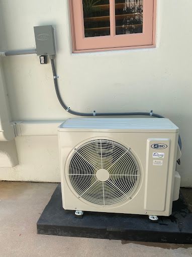 A white air conditioner is mounted on the side of a building next to a window.