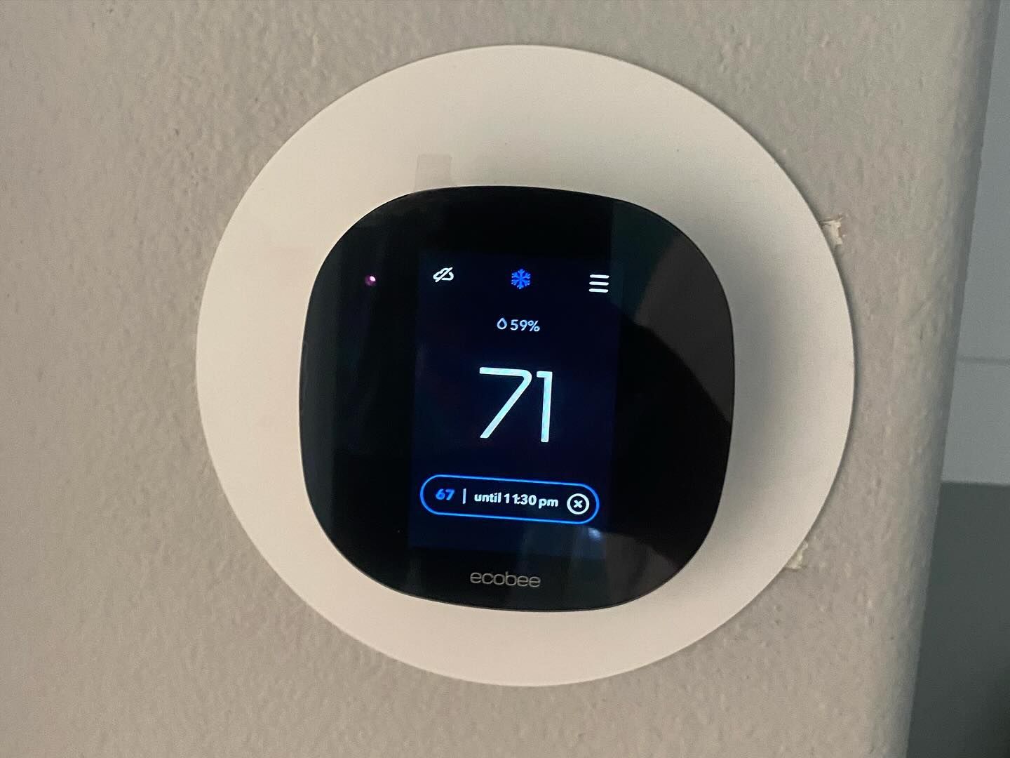 A thermostat is hanging on a wall and the temperature is 71 degrees