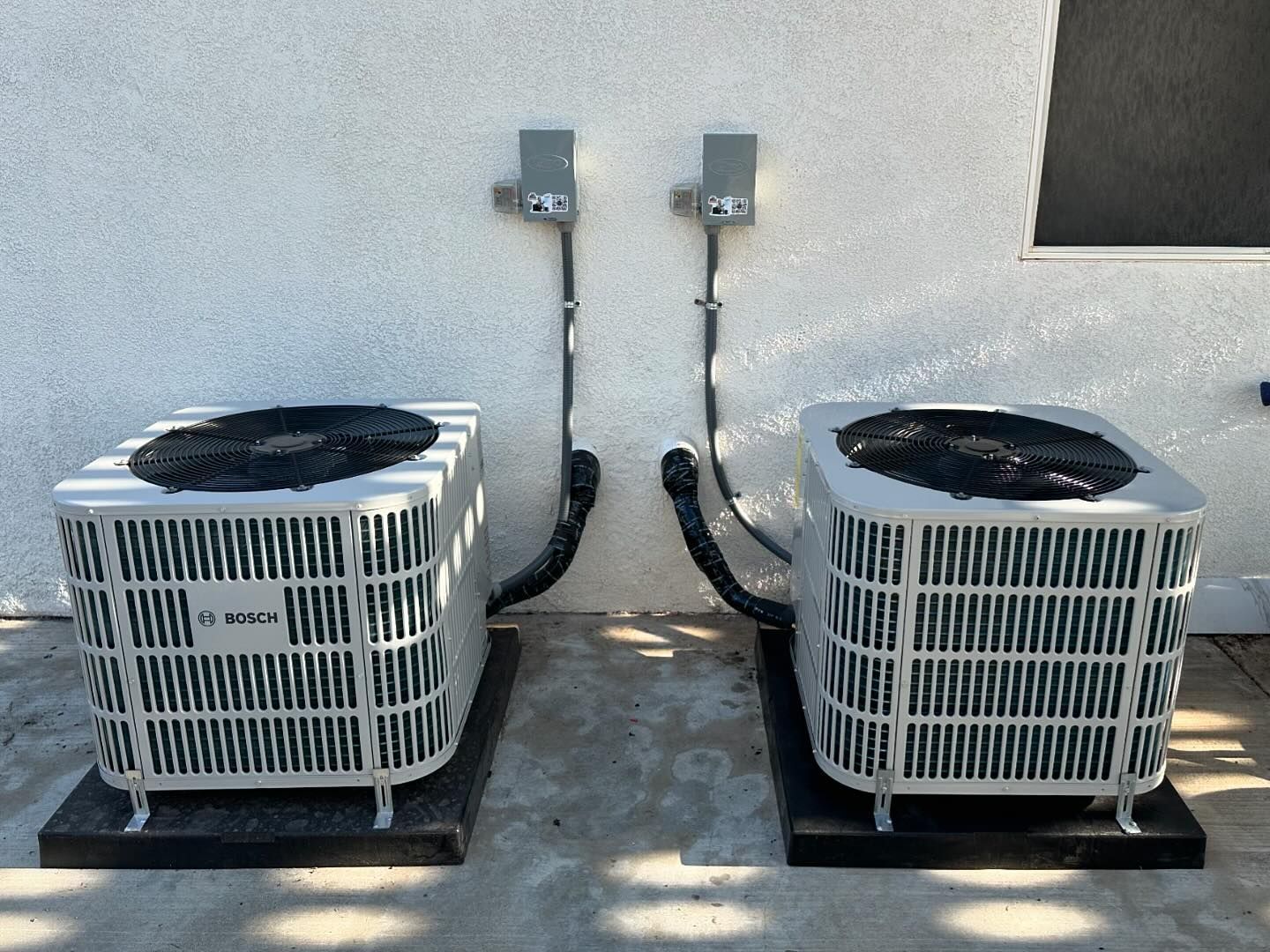 Two air conditioners are sitting next to each other on the side of a building.
