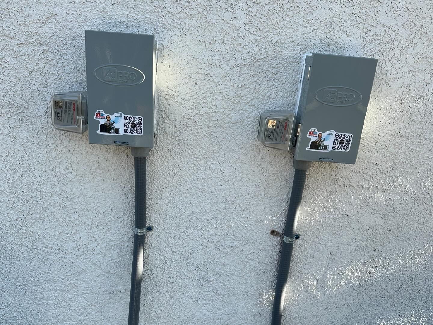 Two electrical boxes are attached to a white wall.
