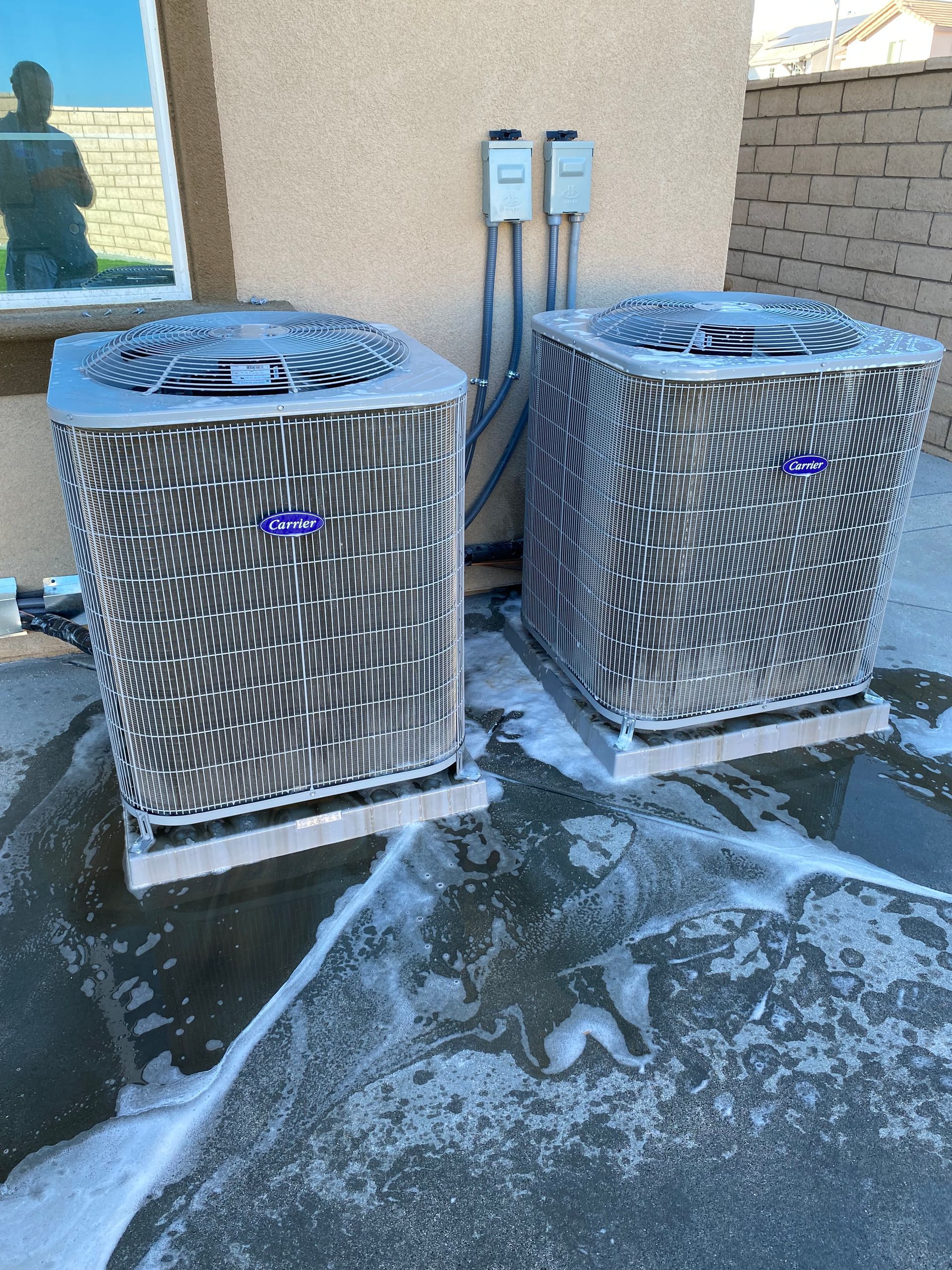 Two air conditioners are sitting next to each other on the side of a building.