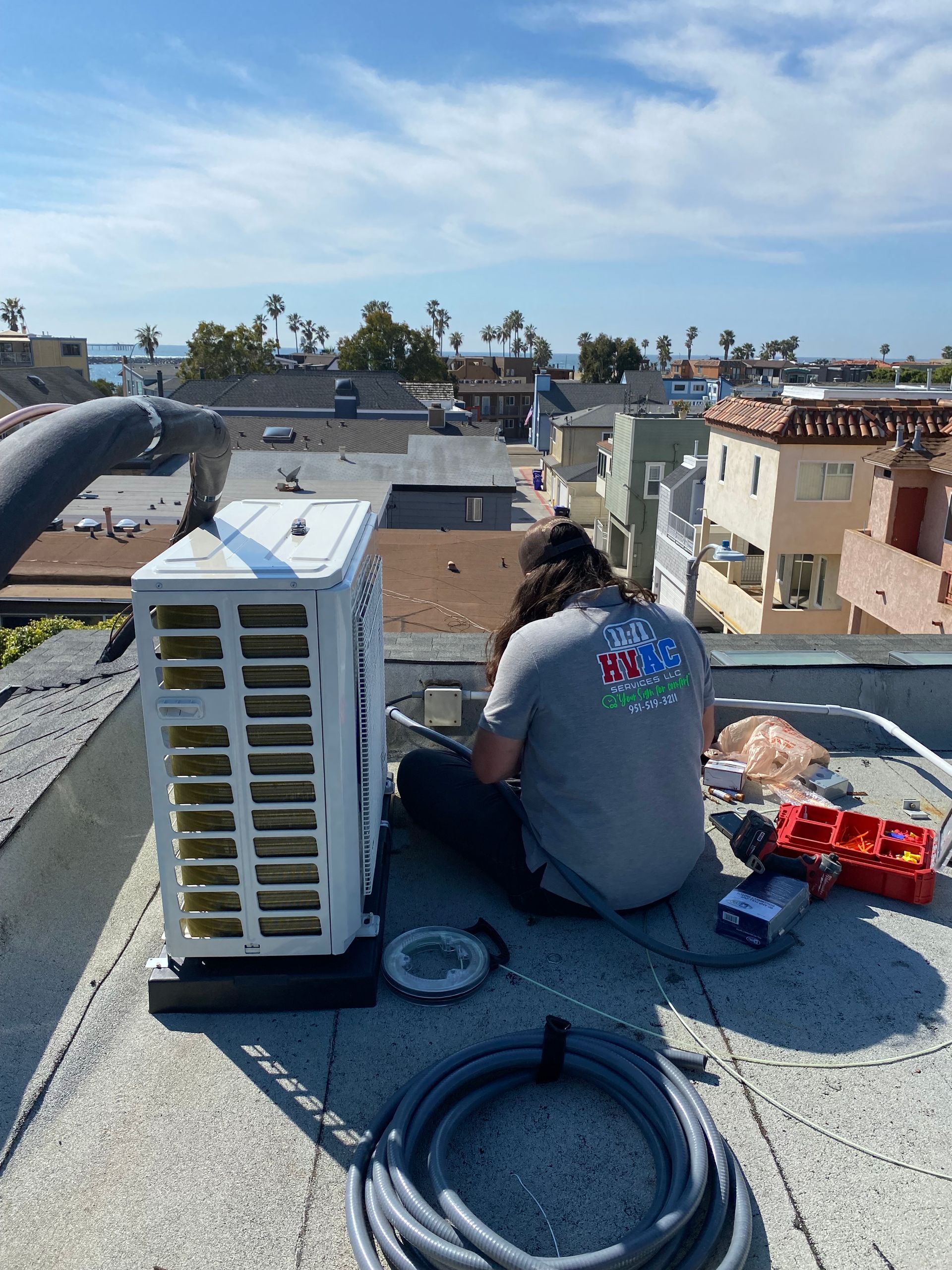 A man is working on an air conditioner on the roof of a building.