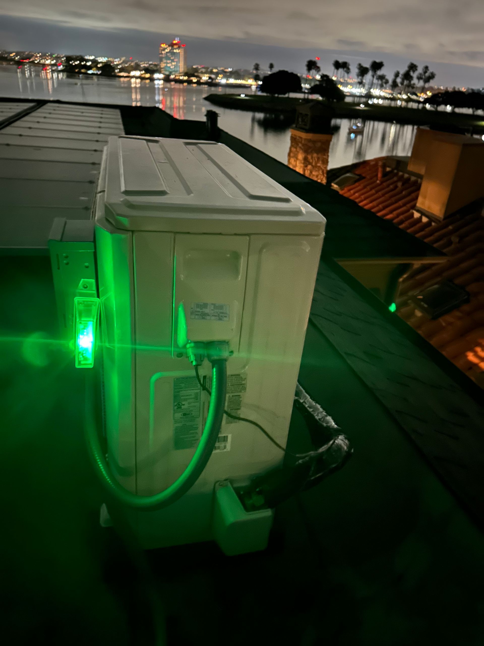A green light is shining on an air conditioner on a roof.