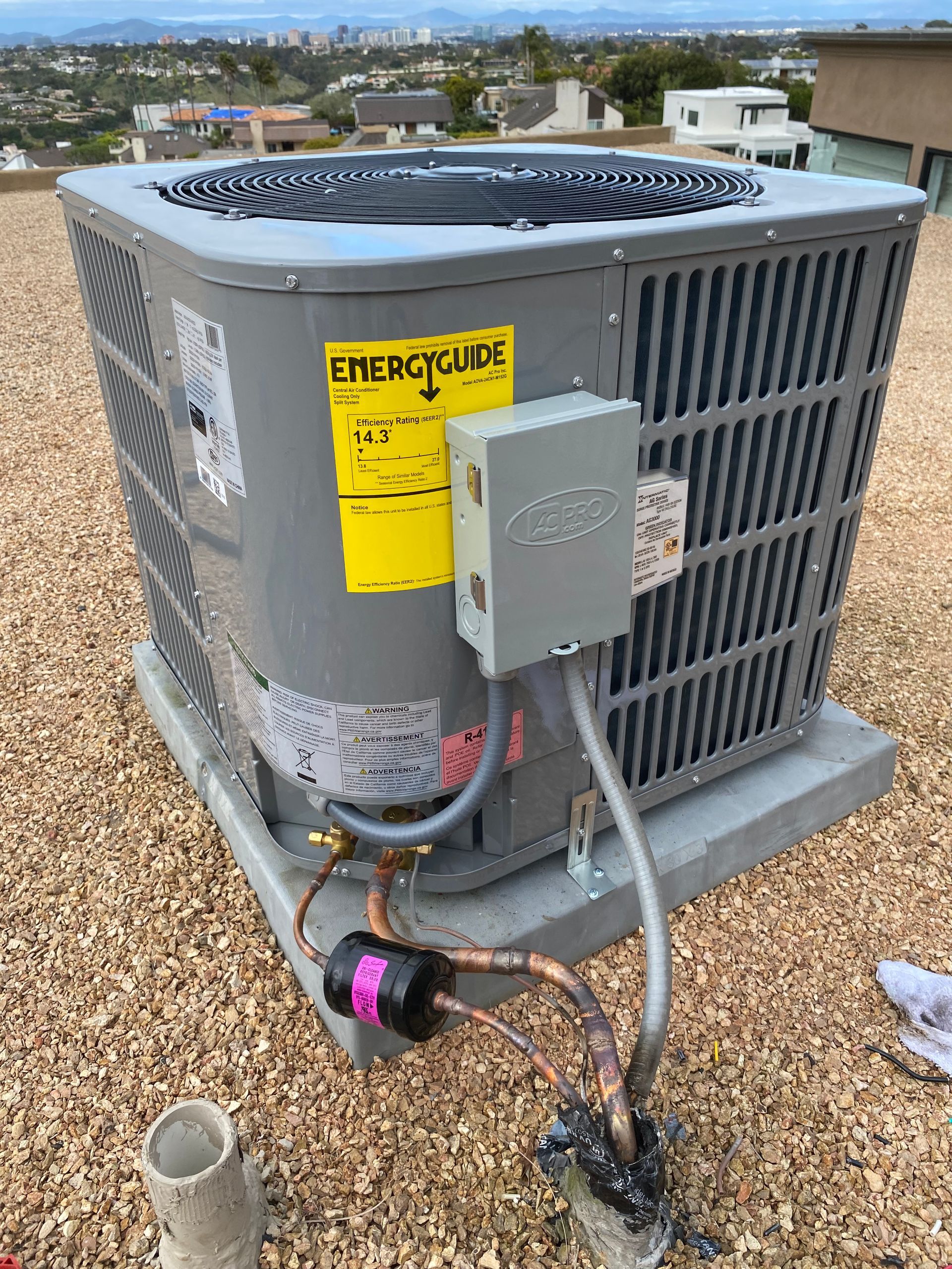 A large air conditioner is sitting on top of a gravel covered roof.